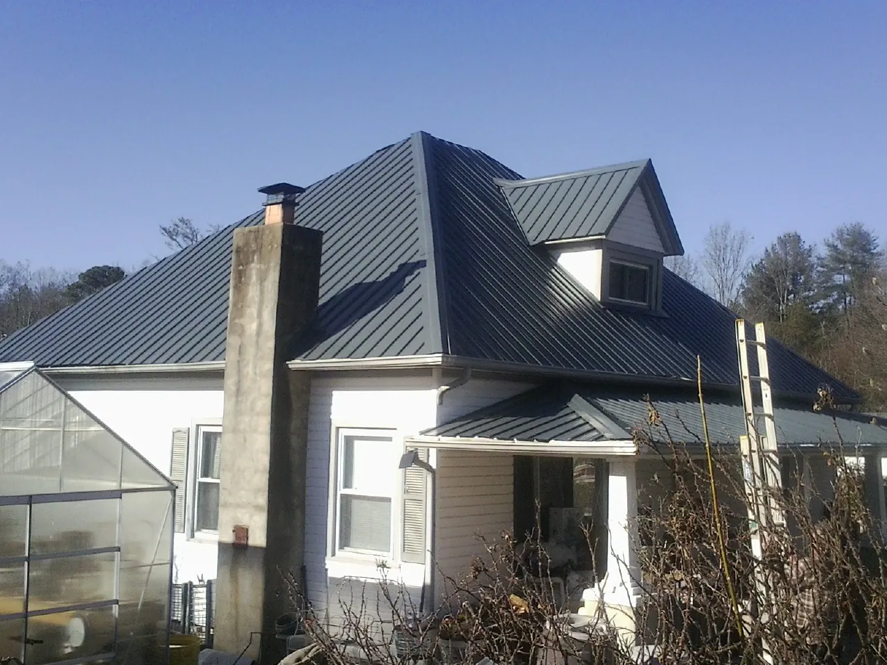 Dark blue standing seam metal roof on a white farmhouse with dormer — Slate & Tile Roof Repair by Roofing Brothers in Collbran