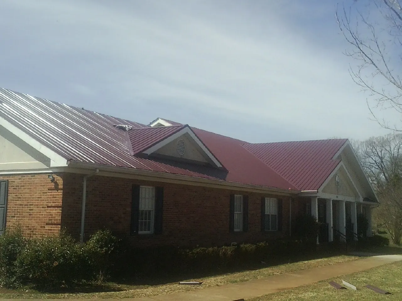 Red metal roof with gabled entries on a long brick building, from a Hail Damage Roof Repair job in Collbran