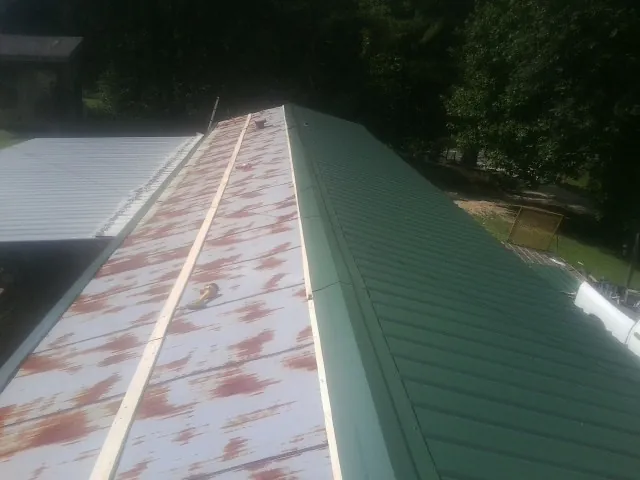 Old rusted panels beside newly installed green metal roofing — Wind Damage Roof Repair by Roofing Brothers in Collbran