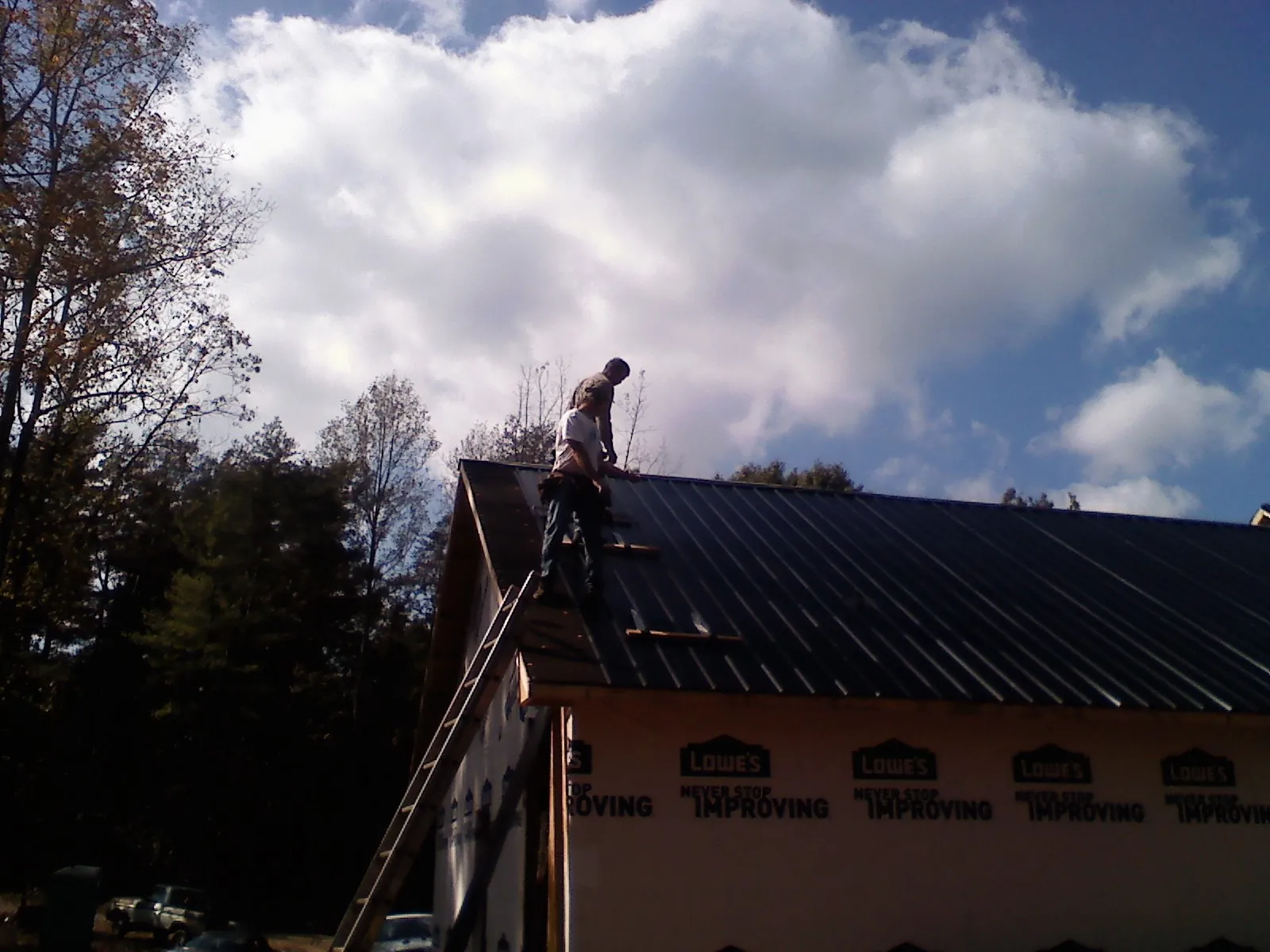 Roofer fastening dark metal panels high against a cloudy sky in Collbran