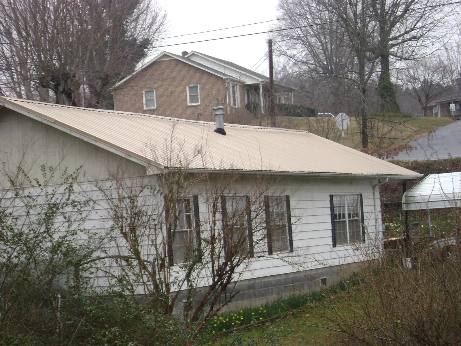 Tan metal roof on a white sided house set into a hillside — Commercial Roofing by Roofing Brothers in Collbran